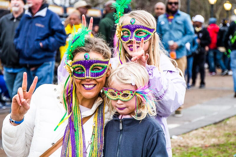 woman and two girls wearing purple masks at mardi gras