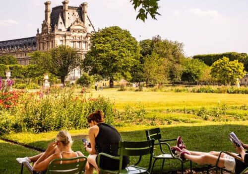 people sitting on chairs in Tuileries garden looking at louvre