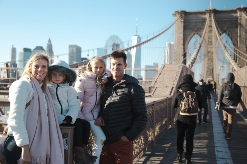 fmaily posing on brooklyn bridge with NYC skyline in background